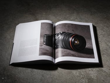 Finished editorial publication open on a concrete surface under controlled studio strobe light, single copy precisely centered, deep shadows framing the edges, minimal background