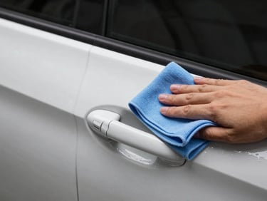Close-up side-angle shot of a car door panel being detailed, microfibre cloth in motion, even workshop lighting illuminating paintwork clarity, no people visible beyond hands, no lifestyle posing