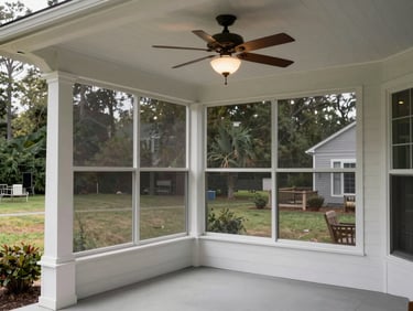Environmental daylight photograph of a finished screened porch addition on a suburban Delaware home — white-painted columns, ceiling fan, view through the screen to the backyard, soft overcast light
