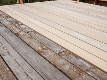 Close wide-angle daylight photo of a deck repair in progress — new composite boards installed alongside original boards, visible contrast between weathered and fresh material, no people, natural overcast light
