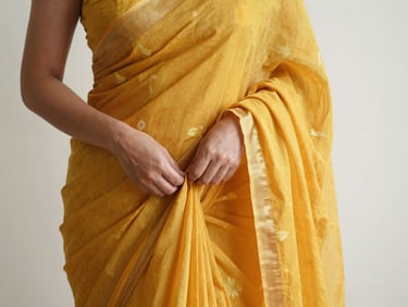 A woman adjusting the pleats of a marigold yellow georgette saree, warm lighting, focus on the fabric drape and hand movement.