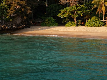 A secluded private beach cove in Thailand, calm turquoise water, warm golden-hour light, 35mm lens