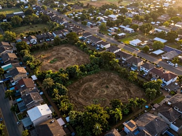 Aerial view of Adjiringanor — semi-rural premium fringe neighbourhood, large undeveloped land parcels alongside newly completed gated compounds, lush vegetation, golden-hour light raking across the roofline