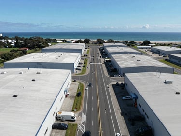 Panoramic aerial of Spintex Road corridor — large industrial and commercial warehouse plots flanking the dual carriageway, Atlantic coastline visible to the south, clear daylight