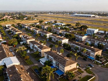 Aerial view of Airport Residential Area showing orderly compound rooftops, embassy row greenery, and the proximity to Kotoka International Airport in the far distance, golden-hour light