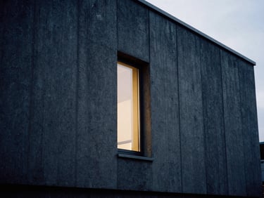 Monolithic concrete building facade with clean vertical lines, soft side-lit window light, high contrast