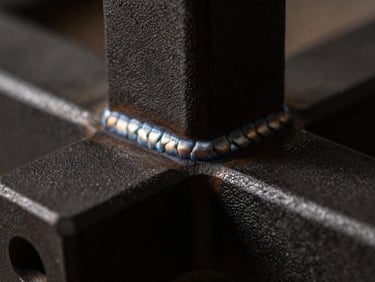 Close-up of a textured matte black powder-coated steel joint, precise weld seam, dramatic side-lighting, dark charcoal tones, 35mm