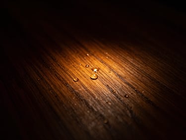Macro shot of a dark oak wood grain glowing with warm amber light from beneath, water droplets evaporating slightly, dark low-key editorial photography, 35mm