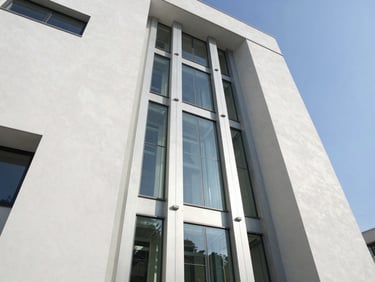Wide-angle architectural perspective of a clean glass elevator shaft in a modern sunlit building, sharp shadows, crisp daylight
