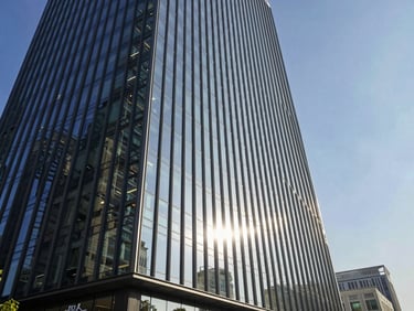 Wide-angle shot of modern glass office building exterior reflecting bright morning sun and clear blue sky