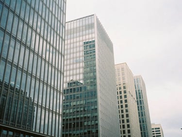 Wide-angle architectural film photography of a modern, high-rise business district, clean glass facades reflecting the overcast sky, desaturated cool tones, 35mm wide-angle.