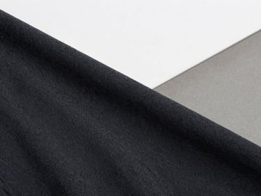 Close-up of heavyweight dark charcoal cotton fabric texture, sharp overcast daylight, architectural framing, 35mm