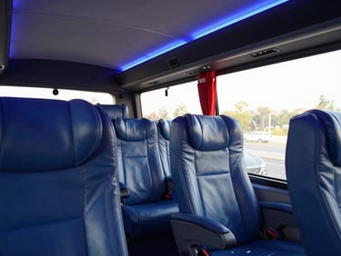 Interior of a premium executive bus, pristine clean leather seats, ambient blue lighting, warm daylight coming through the window.