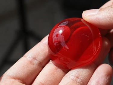 Close-up of a hand holding a transparent red diffusion gel against a studio light, showing texture and light refraction, sharp shadows, realistic workshop ambient light, crisp depth of field, 35mm.