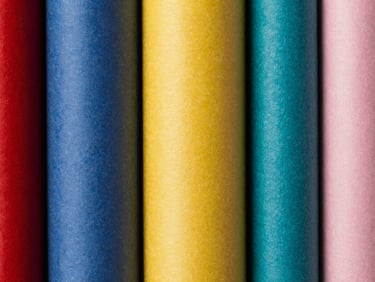 Tight macro shot of a stack of seamless paper rolls in various colors, textured surface, sharp high-contrast studio light, rich saturated colors, crisp depth of field, 35mm.