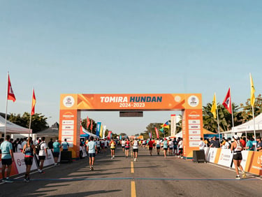 Large-scale outdoor marathon finish line, towering custom archway, flags blowing in the wind, bright clear daylight