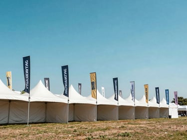 Heavy-duty custom printed event tents and wind-resistant feather flags standing under a bright blue sky, wide environmental shot