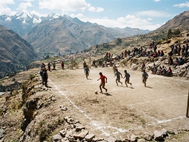Wide-angle documentary shot of a rustic dirt soccer pitch carved into a high-altitude Andean mountain slope, natural harsh daylight, dusty earth tones, 35mm film texture.
