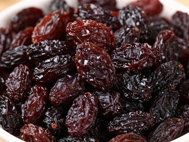 Heap of dark, plump raisins, glistening slightly, in a clean bowl under natural light