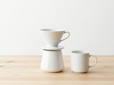 Minimalist ceramic coffee dripper and white mug on a clean wooden tabletop, bright natural morning light