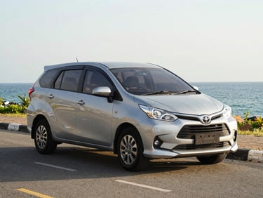 A clean silver Toyota Avanza parked on a paved street in Kupang, bright daylight, professional automotive shot