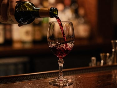 Close-up of red wine being poured into a crystal glass at a dark bar counter, warm amber spotlights, shallow depth of field, moody editorial.