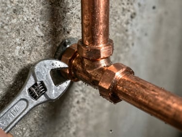 Close-up of burst copper pipe mid-repair, water still beading on the surface, plumber's wrench gripping the fitting, concrete basement wall behind