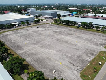Wide aerial drone shot of a flat cleared industrial lot in Johor Bahru, lot boundary markers visible, surrounding industrial estate in background, overcast natural daylight