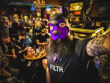 Man in a pup mask, standing in a pub taking a selfie.