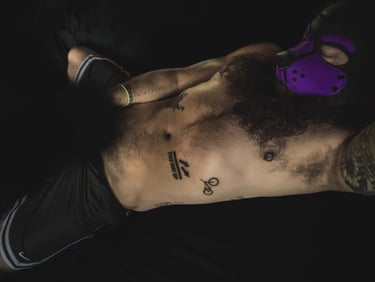 Shirtless man in pup mask, lying in bed in an intimate pose