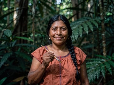 Portrait of Maria Flores, a Shipibo artist, smiling gently while holding a paintbrush, dappled rainforest sunlight, moody documentary photography.