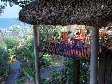 A couple having a romantic dinner in a treehouse-style balcony overlooking tropical greenery