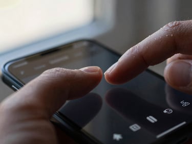 Extreme close-up of a thumb resting on an Android phone screen mid-interaction, UI navigation elements visible on the display, natural window light, shallow depth of field on the hand