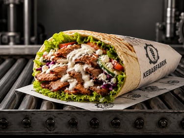 Grilled beef kebab wrap with white sauce, lettuce, and feta cheese on a metal conveyor belt.