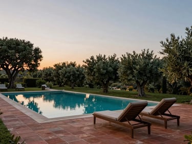 Wide shot of a private villa infinity pool at dusk, two empty loungers, terracotta tiles catching last light, dense olive grove in the background, nobody present, serene and exclusive