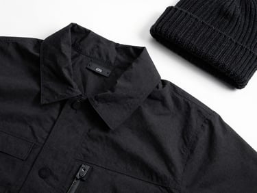 Minimalist flat-lay of a custom technical jacket and a knitted beanie, high-contrast lighting, sharp details.