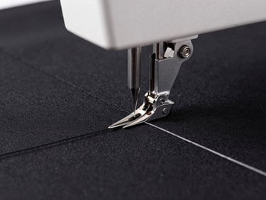 Close-up of a high-speed embroidery machine needle punching thick thread into black fabric, sharp focus