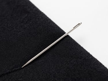 Macro shot of silver embroidery needles threading thick black organic cotton fabric, sharp focus, industrial minimalist studio lighting.
