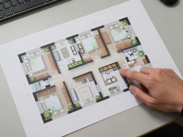 Wide architectural overhead composition of a BPEC Village floor plan layout, printed sheet on a flat table under diffused office lighting, a hand pointing to a suite boundary, neutral background, shot from directly above