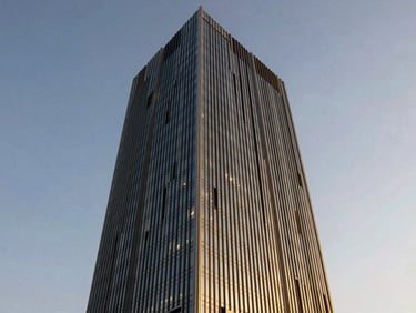 Silueta de un rascacielos moderno al atardecer, con reflejos dorados y azules en los cristales, una luz suave y estratégica iluminando la fachada, perspectiva de bajo ángulo que enfatiza la altura.