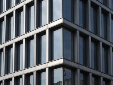 Architectural photograph of a modern building facade with structural glazing, clean minimalist profiles, sharp natural light, deep charcoal and metallic silver tones, high-contrast