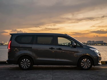 Side profile of a polished dark gray Hyundai Starex parked under golden hour light near the Johor Strait, clean reflective surfaces.