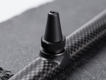 Sleek black tubeless valve stem mounted on a deep-section carbon rim, macro depth of field