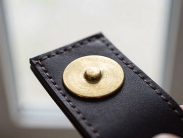 Macro shot of a brass serial plate hand-stitched onto a dark leather label, soft overcast daylight, shallow depth of field