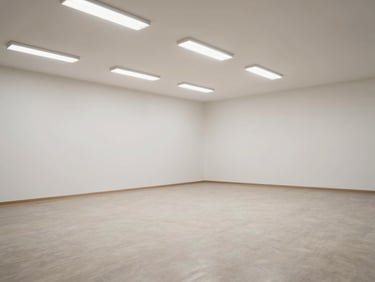 Wide shot of a bare empty event hall with plain white walls, neutral floors, no decoration, harsh overhead fluorescent light — the raw space before any styling begins, open and austere