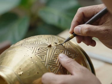 Close-up of a craftsman's hands carving intricate geometric patterns onto a warm brass vessel, soft workshop light, brass shavings visible