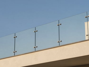 Minimalist glass railing on a modern villa balcony, clean metal brackets, reflecting clear blue sky.