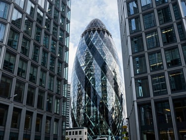 Wide environmental shot of a modern glass-and-steel business hub in London, cool-toned daylight, sharp contrast, deep blue and slate tones, 35mm lens.