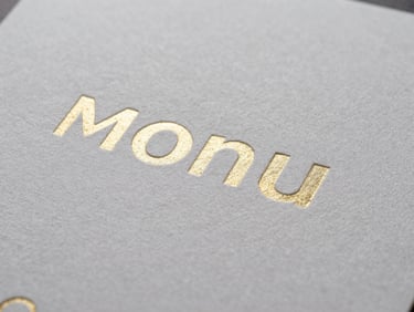 Macro shot of a velvet-laminated menu with spot UV text, emphasizing texture and finish, sharp studio lighting, high contrast, industrial precision.