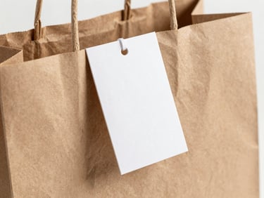 Close-up of a custom-printed paper shopping bag with a branded clothing tag attached, showing textured paper and crisp ink, studio lighting.